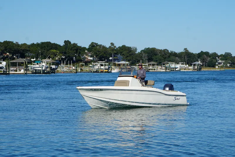 Slide: The Image of 2016 Scout 210 XSF boat cruising on a calm lake with scenic shoreline. - 6