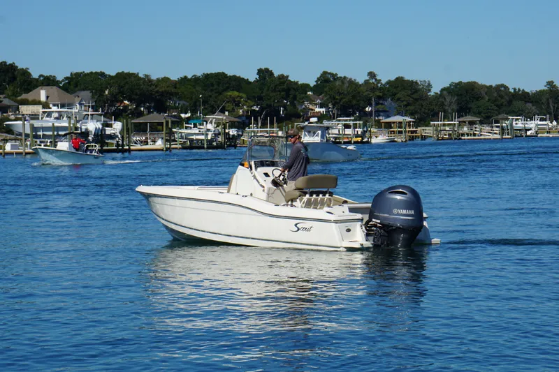 Slide: The Image of 2016 Scout 210 XSF boat cruising on a calm blue lake near a marina. - 5