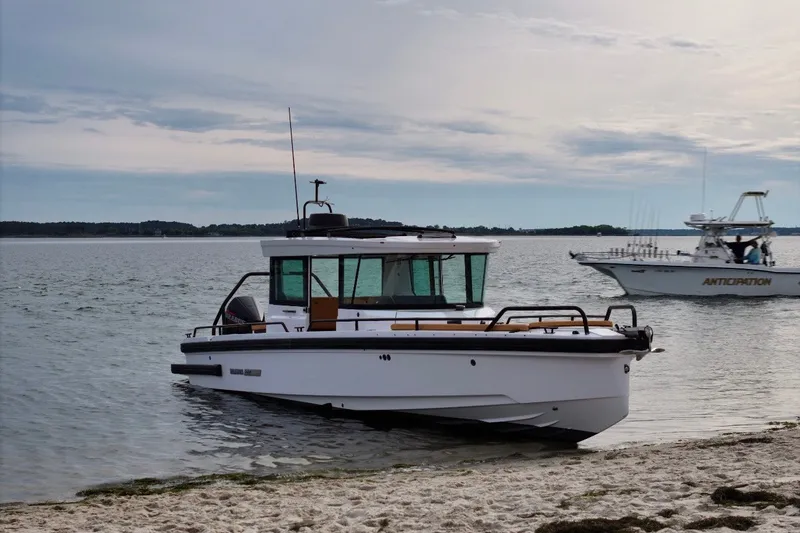 Slide: The Image of 2021 Axopar Brabus 28 Cabin boat docked on a sandy shore with another boat nearby. - 10