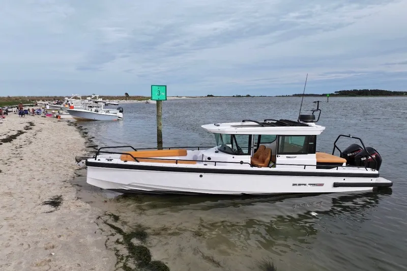 Slide: The Image of 2021 Axopar Brabus 28 Cabin boat docked on a sandy beach. - 6