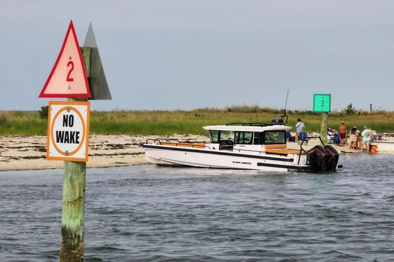 Slide: The Image of 2021 Axopar Brabus 28 Cabin near a "No Wake" sign by the shore. - 4