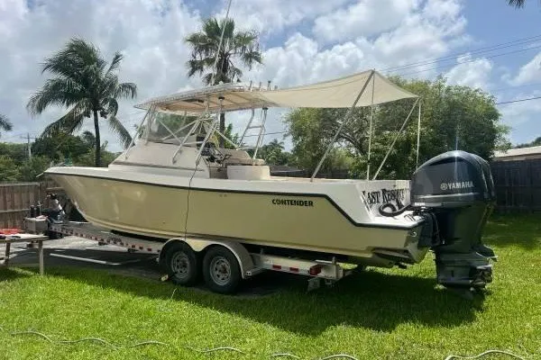Slide: The Image of 2004 Contender 31 Fisharound boat on trailer, parked in a grassy yard with palm trees. - 1