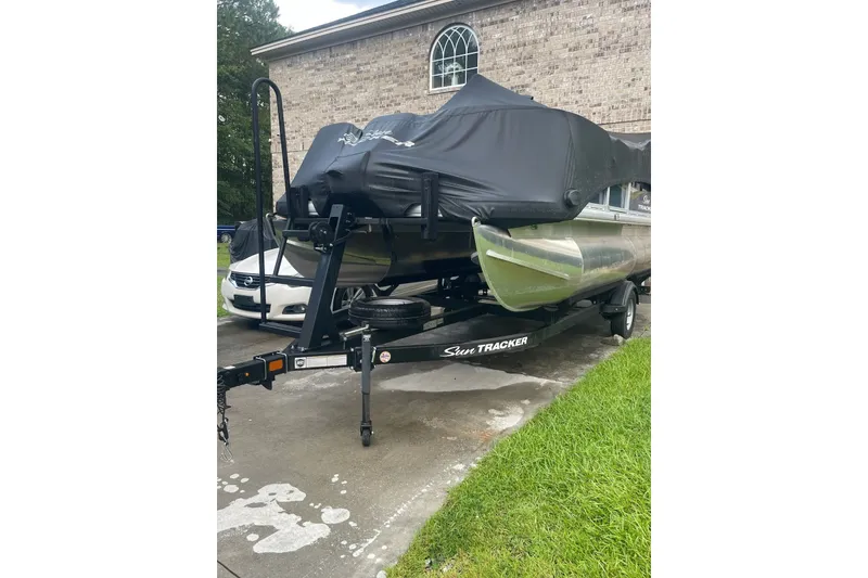 The Image of 2025 Sun Tracker Bass Buggy 18 Classic Series pontoon boat on trailer, covered and parked. - 0
