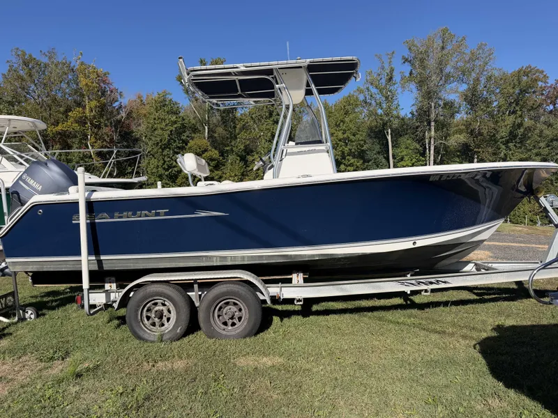 The Image of A blue 2013 Sea Hunt Ultra 225 boat on a trailer, surrounded by trees. - 0