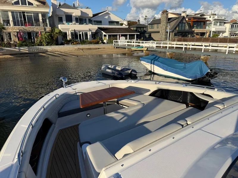 Slide: The Image of The image shows the bow of a 2022 Sea Ray Sundancer 370 Outboard, featuring a wooden table and cushioned seating. Houses and boats are visible in the background. - 42