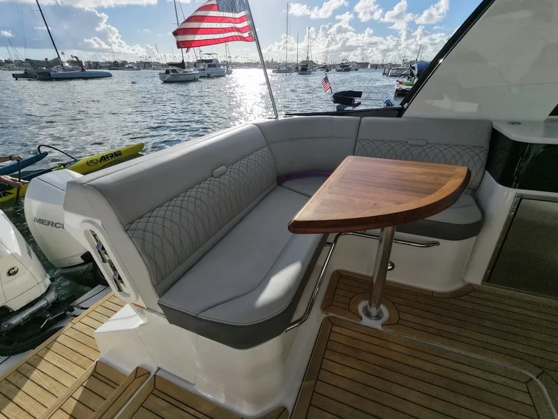Slide: The Image of The image shows the aft of a Sea Ray Sundancer 370 Outboard with a cozy seating area and wooden table. Boats are visible on the water in the background. - 19