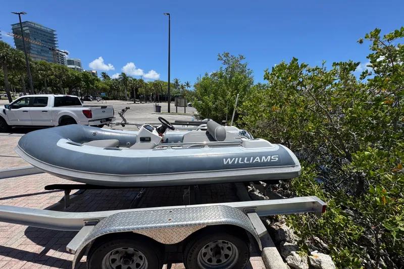 Slide: The Image of 2019 Williams Jet Tenders Sportjet 345 on trailer, parked near greenery and vehicles. - 1