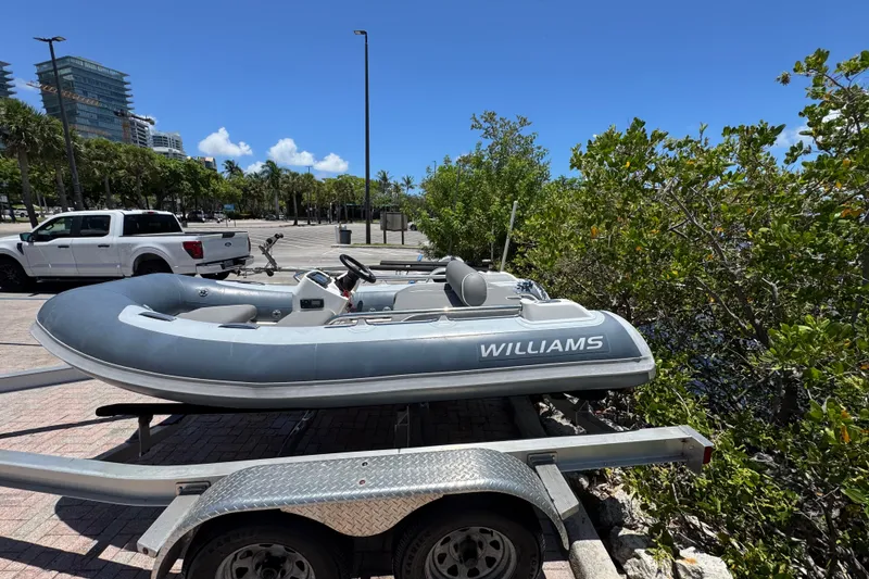 Slide: The Image of 2019 Williams Jet Tenders Sportjet 345 on trailer, parked near greenery and urban backdrop. - 2