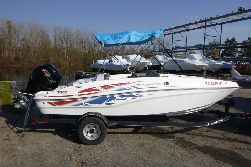 The Image of 2022 Tahoe T18 boat with blue canopy on trailer, parked near a lake. - 0