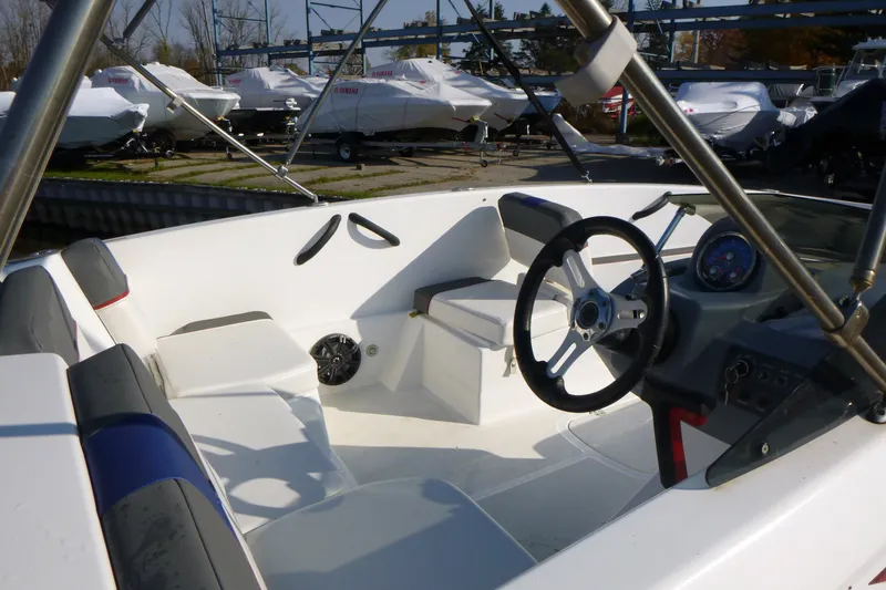 Slide: The Image of 2022 Tahoe T18 boat interior with steering wheel and seating, docked near covered boats. - 14