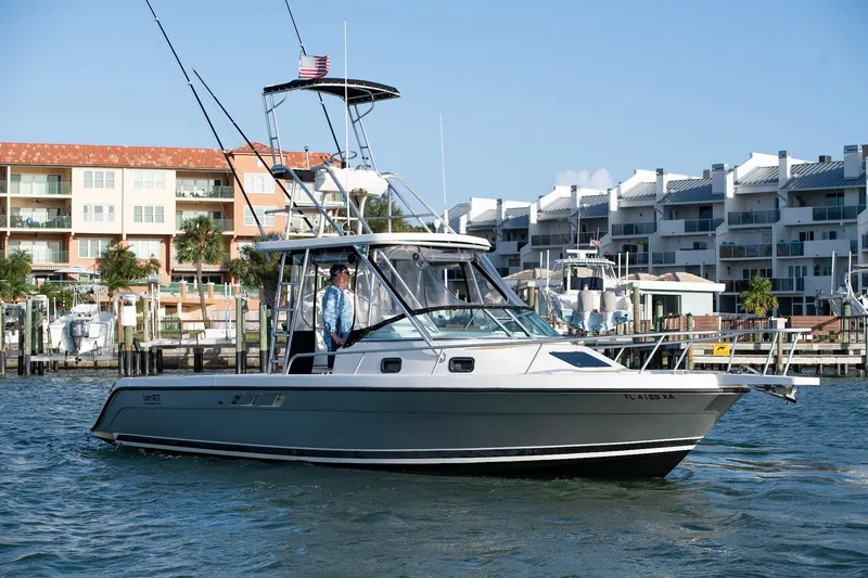 Slide: The Image of 1992 Luhrs Tournament 300 boat cruising near waterfront buildings, featuring fishing rods and American flag. - 4
