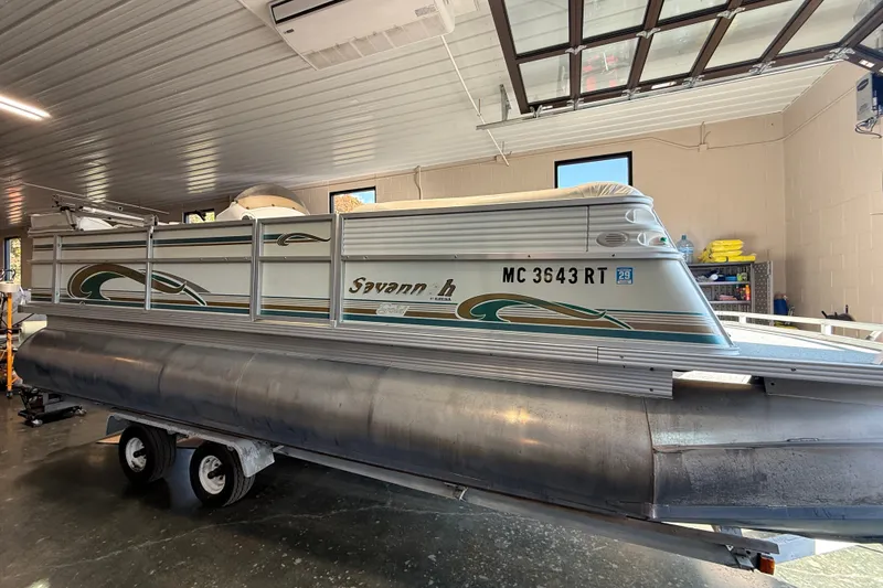 The Image of 1999 Crest 22 Savannah pontoon boat in a garage, showcasing side view and trailer. - 0