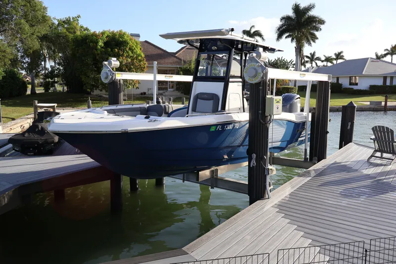 Slide: The Image of 2023 NauticStar 251 Hybrid boat on lift at waterfront dock, surrounded by palm trees. - 48