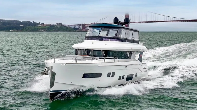 Slide: The Image of A 2020 Sirena 64 yacht cruising on the water with a bridge in the background. - 2