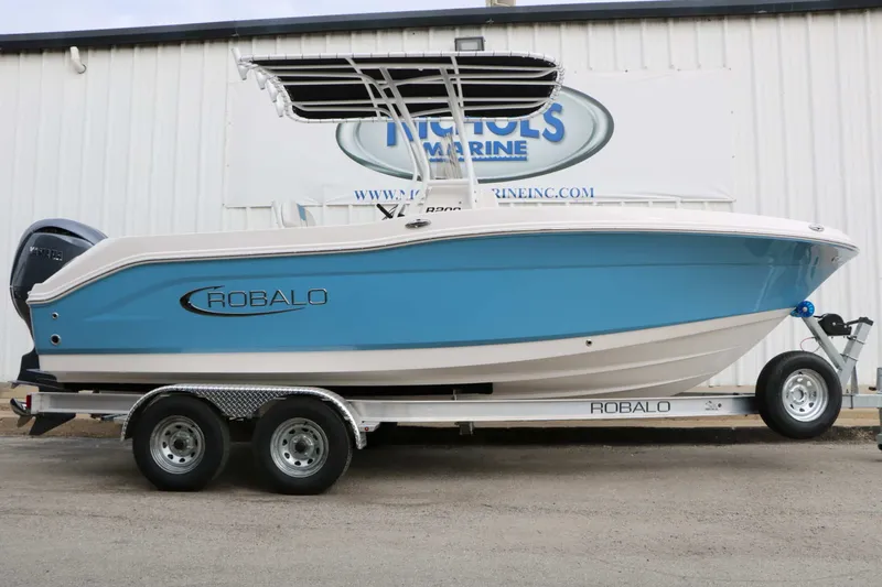 Slide: The Image of A 2027 Robalo R200 Center Console boat on a trailer, featuring a blue hull and black T-top. - 2