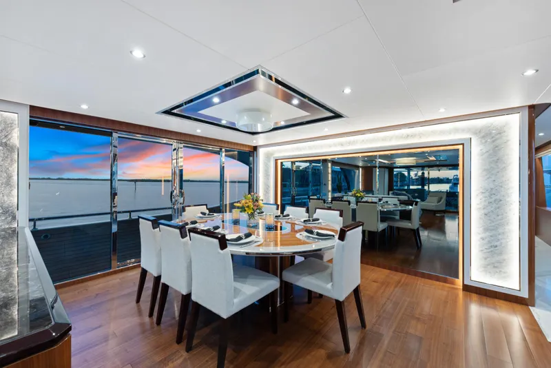 Slide: The Image of Luxuriöser Speisesaal auf einer Yacht mit Holzboden, eleganten weißen Stühlen und großen Fenstern mit Blick auf den Sonnenuntergang. - 13