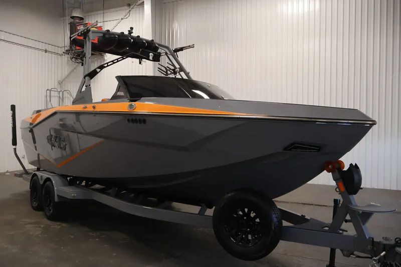 The Image of 2025 Axis T250 boat in a garage, featuring sleek gray and orange design on a trailer. - 0