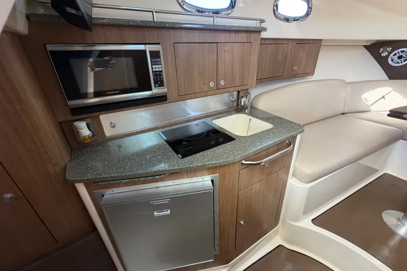 Slide: The Image of 2014 Boston Whaler 315 Conquest interior kitchen with microwave, sink, and seating area. - 45