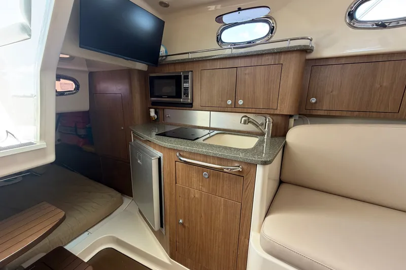 Slide: The Image of 2014 Boston Whaler 315 Conquest cabin interior with kitchenette, microwave, and seating area. - 49