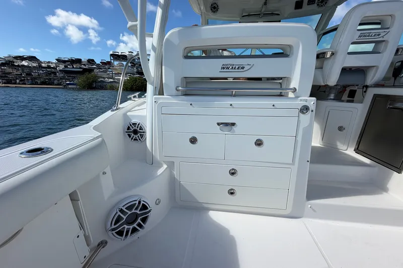 Slide: The Image of 2014 Boston Whaler 315 Conquest interior with storage drawers and seating, docked by the water. - 16