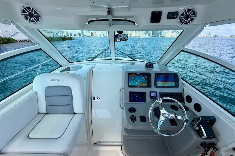 Slide: The Image of 2014 Boston Whaler 315 Conquest helm with navigation screens, steering wheel, and waterfront view. - 26