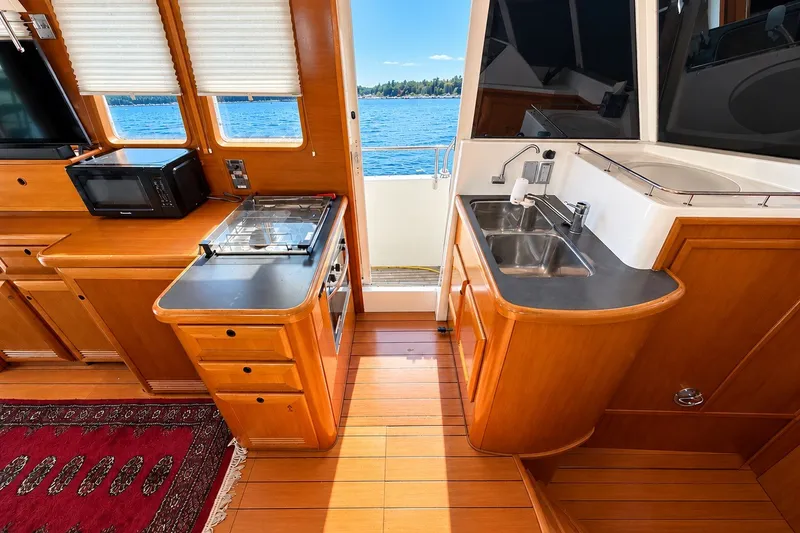 Slide: The Image of 2005 Beneteau Swift Trawler 42 kitchen with wood cabinetry, sink, stove, and microwave, overlooking water. - 14