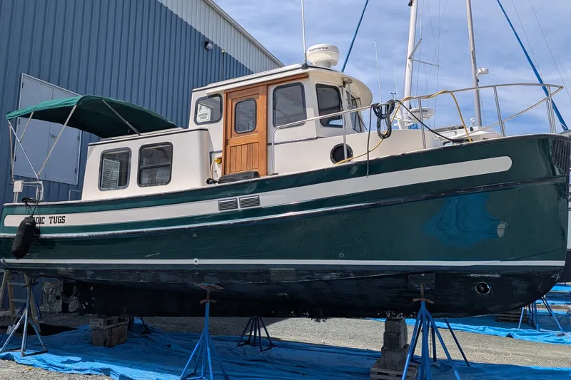 Slide: The Image of 1995 Nordic Tug 26 boat on stands, green hull, docked near blue building. - 43