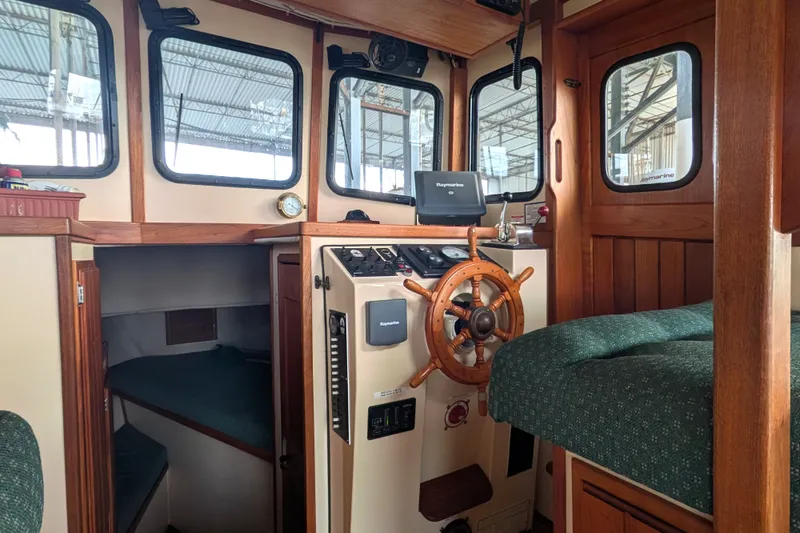 Slide: The Image of Cozy 1995 Nordic Tug 26 interior with helm, wooden accents, and sleeping area. - 19