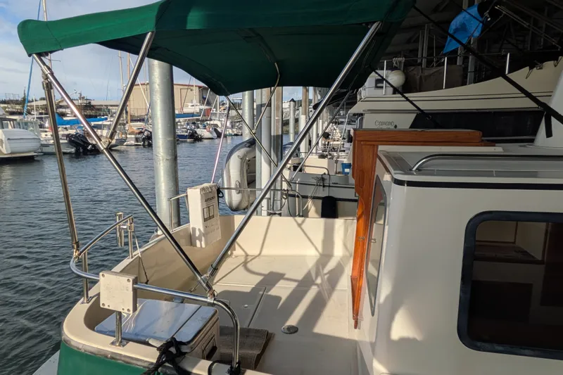 Slide: The Image of 1995 Nordic Tug 26 docked at marina, featuring green canopy and spacious deck area. - 5