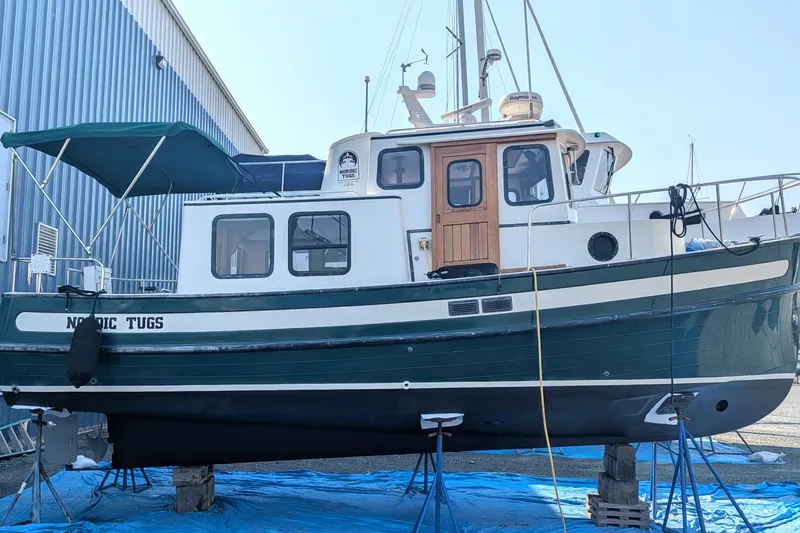 Slide: The Image of 1995 Nordic Tug 26 boat on stands, blue tarp, marina background. - 8