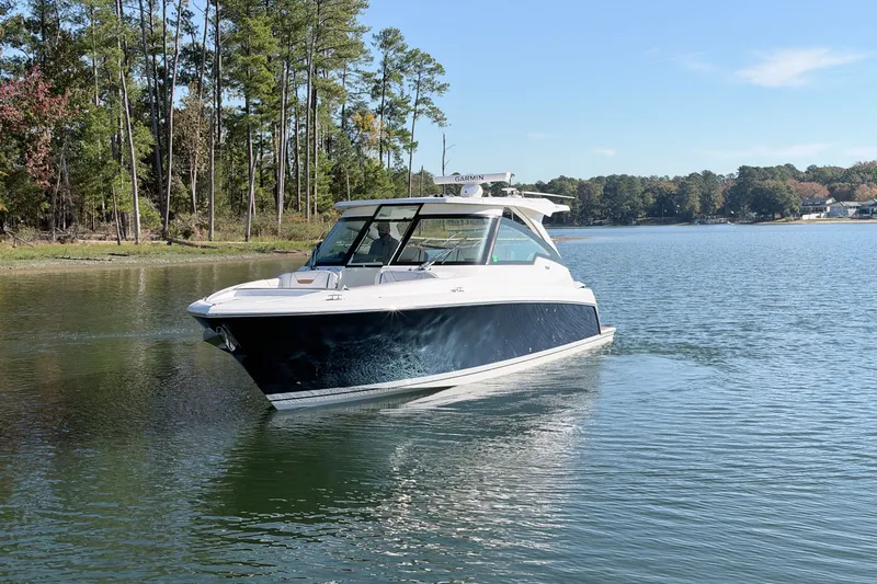 Slide: The Image of 2020 Tiara Sport 34 LX boat cruising on a serene lake with forested shoreline. - 2