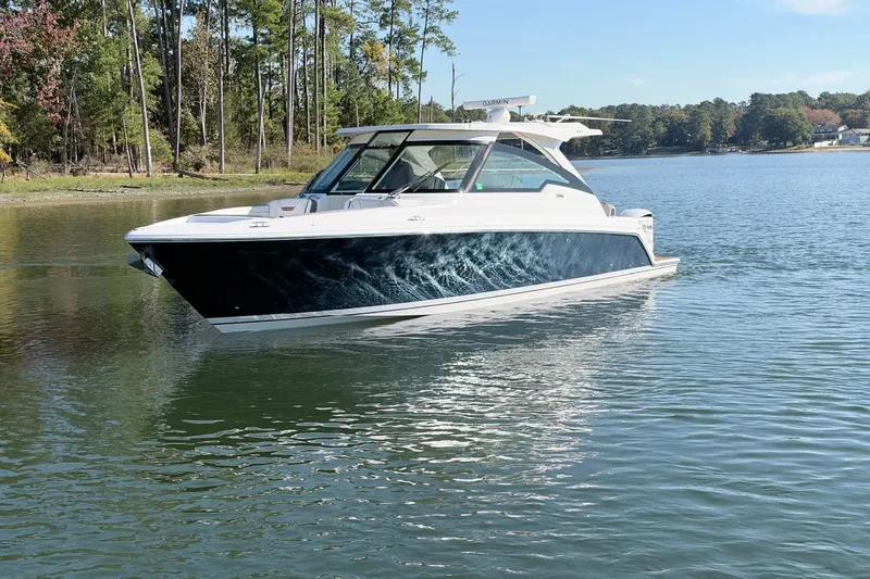 Slide: The Image of 2020 Tiara Sport 34 LX boat cruising on a serene lake with forested shoreline. - 9