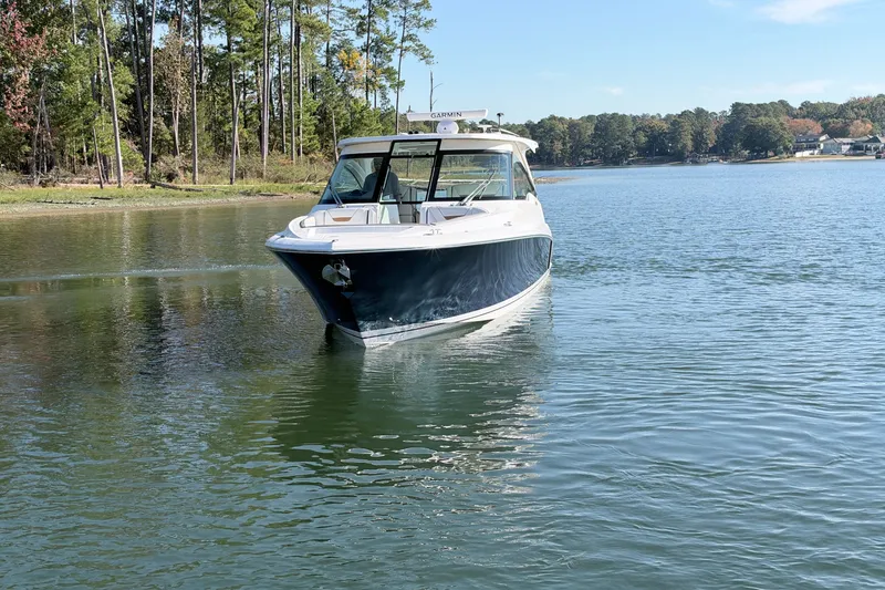 Slide: The Image of 2020 Tiara Sport 34 LX boat cruising on a serene lake with forested shoreline. - 8