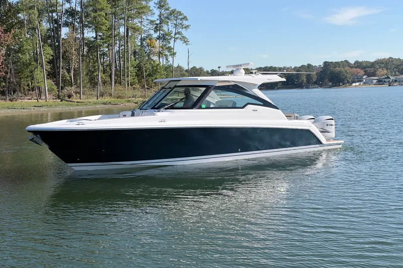 Slide: The Image of 2020 Tiara Sport 34 LX boat cruising on a serene lake with forested shoreline. - 3