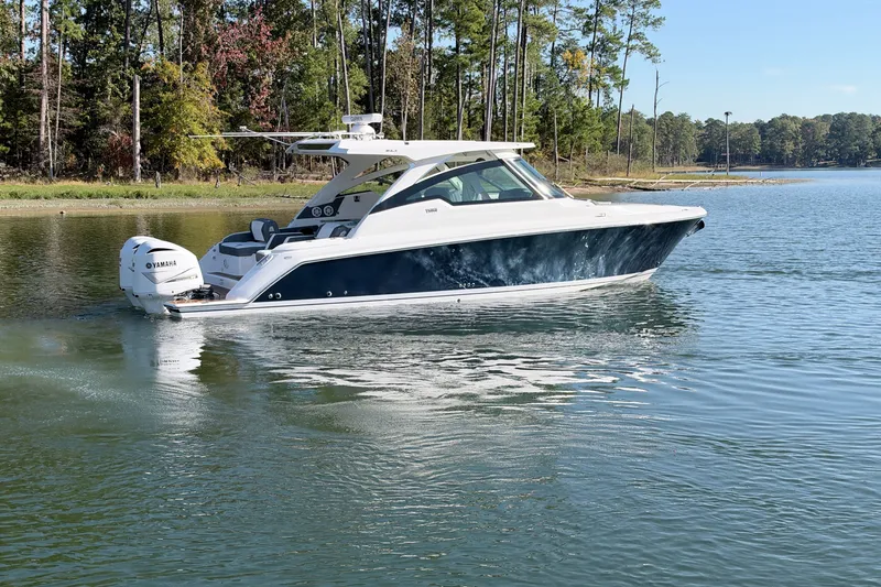 Slide: The Image of 2020 Tiara Sport 34 LX boat cruising on a serene lake with forested shoreline. - 5