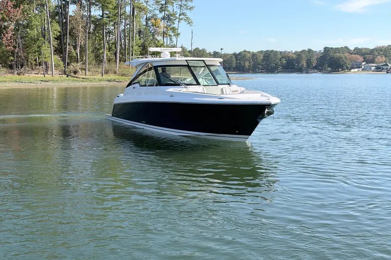 Slide: The Image of 2020 Tiara Sport 34 LX boat cruising on a serene lake with forested shoreline. - 6
