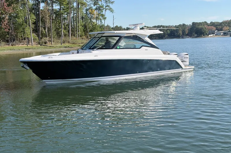 Slide: The Image of 2020 Tiara Sport 34 LX boat cruising on a serene lake with forested shoreline. - 10