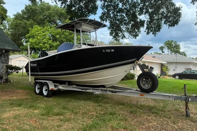 The Image of 2008 Triton 225 CC boat on trailer, parked outdoors near houses and trees. - 0