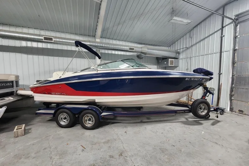 Slide: The Image of 2017 Regal 2300 Bowrider boat in storage, featuring a blue and red exterior. - 2