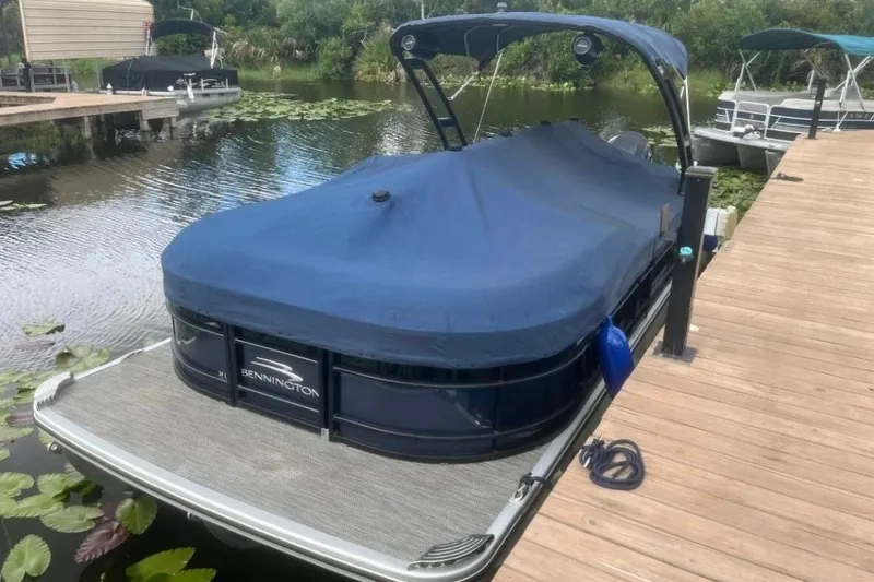Slide: The Image of 2023 Bennington 24 LXS Swingback pontoon boat docked with blue cover. - 3