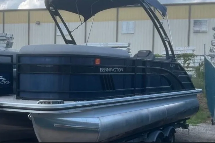Slide: The Image of 2023 Bennington 24 LXS Swingback pontoon boat with canopy, parked outdoors. - 8