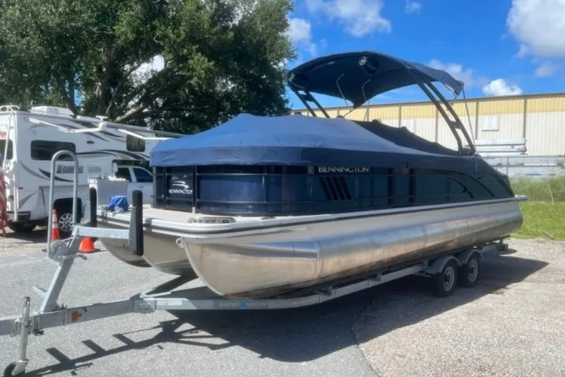 Slide: The Image of 2023 Bennington 24 LXS Swingback pontoon boat on trailer, covered and parked outdoors. - 1