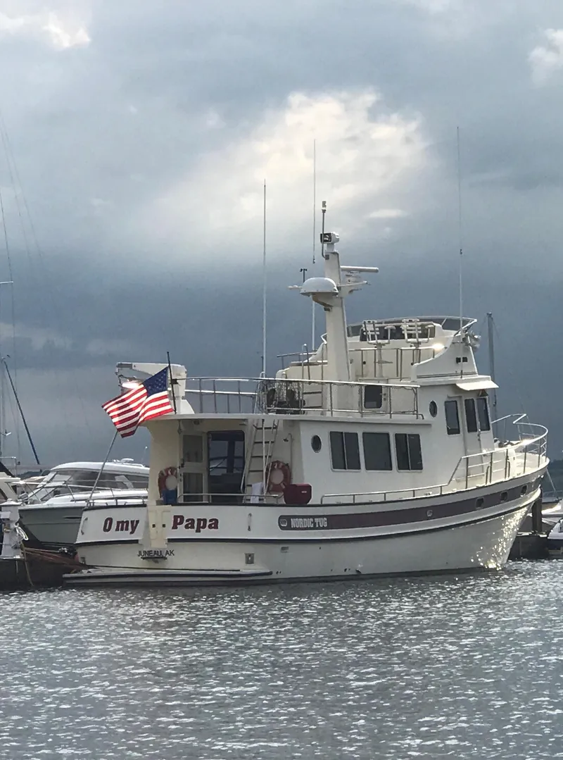 Slide: The Image of Nordic Tug 52 boat from 2003 docked, with American flag, under cloudy sky. - 5