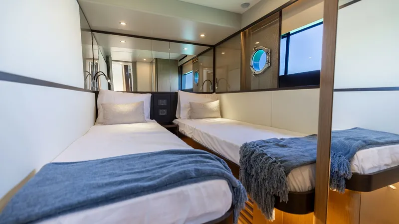 Slide: The Image of Twin Guest Cabin Interior The twin guest cabin of the 2027 Absolute 60 Flybridge exudes modern elegance with its sleek design and inviting ambiance. Featuring two comfortable single beds adorned with plush bedding, the cabin offers ample natural light through a stylish porthole. H - 6492503
