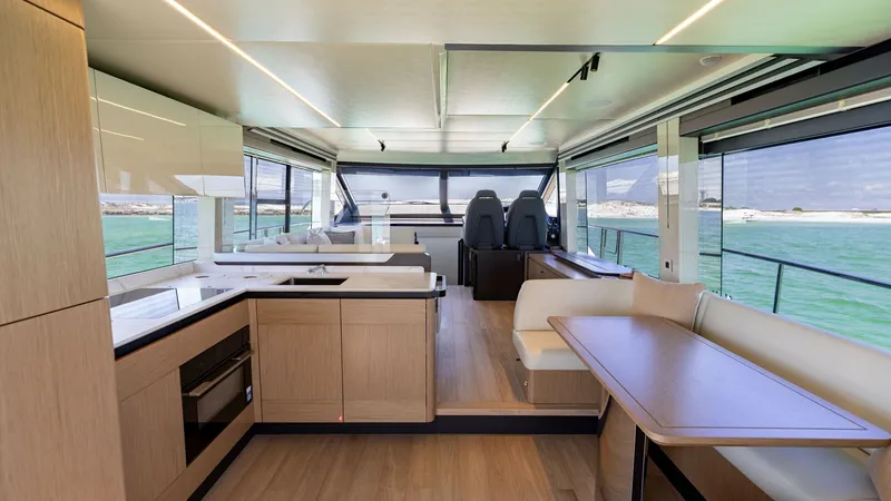 Slide: The Image of Spacious Interior Salon and Helm The interior salon of the 2027 60 Absolute Flybridge showcases a modern and open layout, featuring elegant wood finishes and ample natural light. The space includes a well-equipped galley, a comfortable dining area with plush seating, and expansive window - 6492475