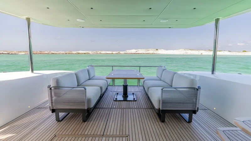 Slide: The Image of Spacious Aft Deck Lounge Area The aft deck of the 2027 60 Absolute Flybridge features a luxurious seating arrangement with plush sofas and a sleek dining table, perfect for alfresco dining and relaxation. The teak flooring enhances the elegance of the space, complementing the panorami - 6492510