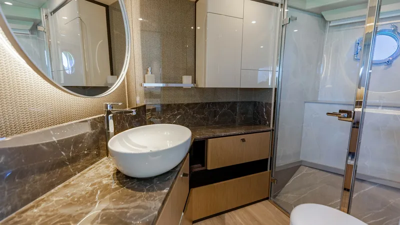 Slide: The Image of Luxurious Master Ensuite Bathroom This elegant ensuite bathroom on the 2027 60 Absolute Flybridge features exquisite marble countertops and a stylish vessel sink. The space is thoughtfully designed with modern cabinetry and a glass-enclosed shower, providing both functionality and luxury. - 6492495