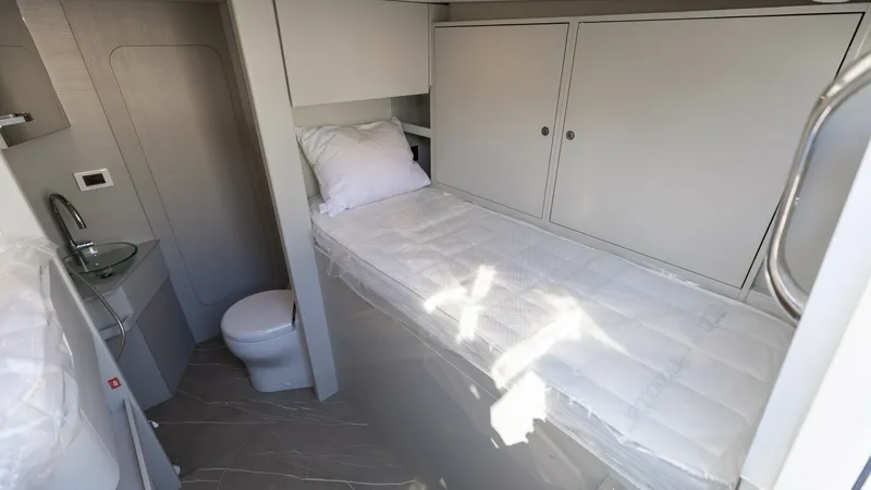 Slide: The Image of Crew Cabin with Ensuite Facilities This crew cabin on the 2027 60 Absolute Flybridge offers a compact and efficient layout, featuring a single bed with storage cabinets overhead. The ensuite facilities include a modern compact toilet and sink, seamlessly integrated into the cabin design. T - 6492543