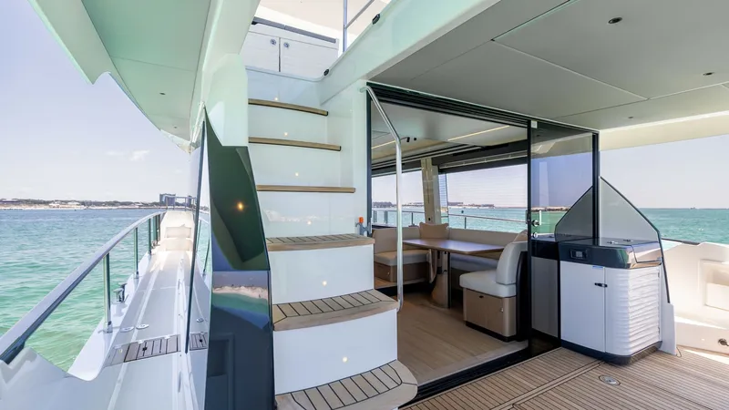 Slide: The Image of Flybridge Access and Aft Deck View This image showcases the elegant flybridge access with sleek teak steps leading upwards, contrasted beautifully against the yacht's modern white exterior. The aft deck features a spacious seating area with ample natural light streaming through large glass - 6492506