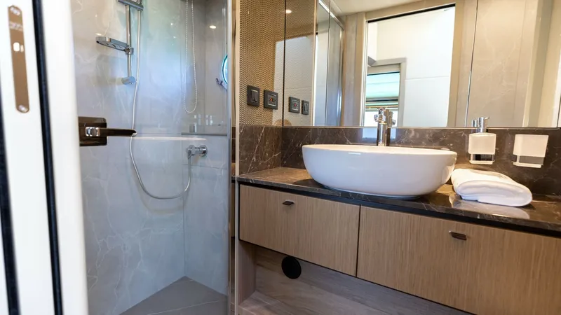 Slide: The Image of Luxurious Ensuite Bathroom This elegant ensuite bathroom on the 2027 60 Absolute Flybridge features a modern design with a spacious glass-enclosed shower and sleek fixtures. The vanity showcases a stylish vessel sink atop a rich, marble countertop, complemented by warm wood cabinet - 6492500